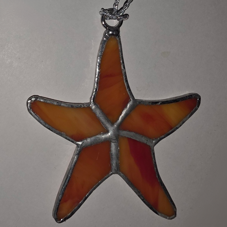 Stained glass starfish pendant in warm sunset colors with silver solder lines.
