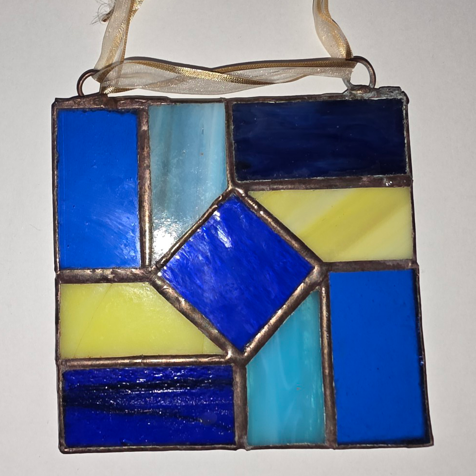 Geometric stained glass suncatcher with blue, aqua, and yellow glass panels and silver solder lines.